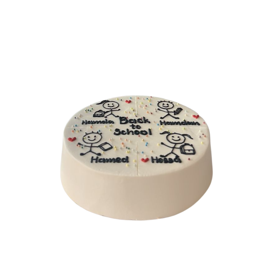 A round white frosted cake with black text reading 'Hummada Bath Is School' and 'Hummada Humsa', decorated with small red hearts, blue and red sprinkles, and simple stick-figure drawings, shown on a plain white background.